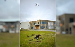 A drone flies in the air and holds a measuring system on a cable above the ground.