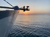 The picture shows part of the ship's bow with the GNSS antenna and two radar sensors. In the background the sun is setting over the lake.