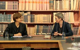 Two women sitting and talking in front of a book shelf in the hitoric library.