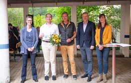 Group photo with five people: The award winner holds a certificate and a bouquet of flowers.