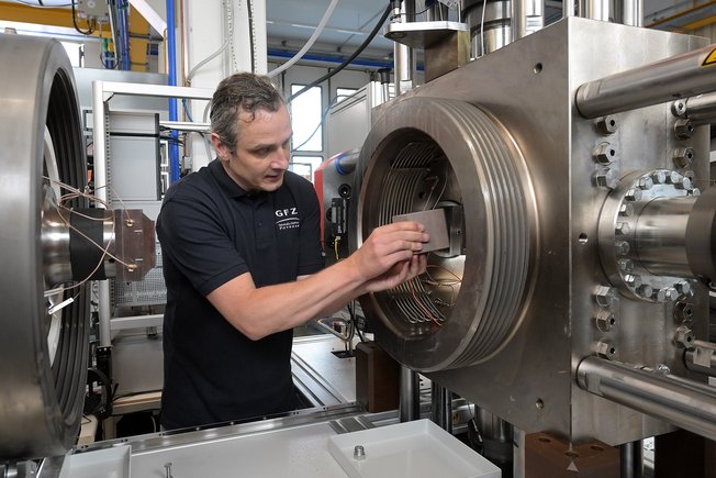 A man stands at the high-pressure unit and inserts a cube-shaped rock sample between the metal plungers of the press.