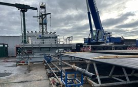 In the background: The drilling tower made of metal struts. Next to it, crane equipment. In the foreground, pipe rods.