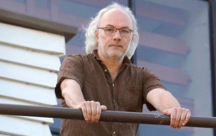 Tassara, weiße Haare, Brille, hält sich an Geländer fest