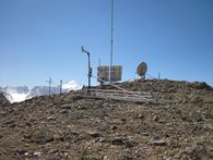 Die Abbildung zeigt die ROMPS am Abramov Gletscher. Im Vordergrund steht ein Schneemesssystem. Dahinter von rechts nach links, die GPS-Antenne, Solarzellen und der Windmast, ein Regensammler und links ein Strahlungssensor und ein Temperaturmessgerät.