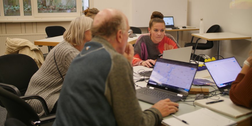 An einem Tisch sitzen mehrere Personen, die an Laptops arbeiten.