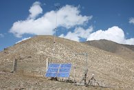 The picture shows a hydrometric measuring station. On the left is a pillar with the GNSS antenna, in the middle are the solar panels, a VSAT station for communication, a 10-meter-high wind mast. To the right of this is a rain collector and in the foreground a snow measuring device.