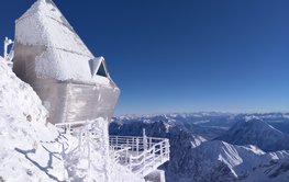 A futuristic-looking silver building with a balcony, above the snow-covered peaks of the Alps.