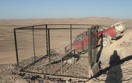 Das Foto zeigt eine umzäunte Solaranlage in einer staubigen Landschaft. Es steht ein Auto hinter dem Zaun