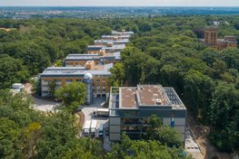 A cube-shaped new building in the foreground, behind it a series of other modern buildings, all surrounded by the forest on Potsdam's Telegrafenberg.