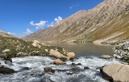 A lake, a foaming tributary in the foreground, bare mountain slopes on the sides.