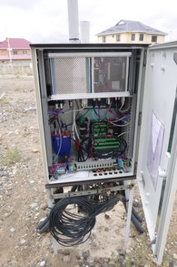 Das Bild zeigt das Innenleben eines ROMPS für eine Hydromet-Station. Oben sind zwei Metallkästen für den PC und die Stromversorgung. Darunter ein VSAT-Modem zur Datenübertragung. Darunter befinden sich ein GNSS-Empfänger und der Datenlogger.