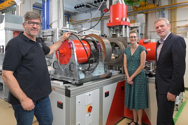 Group photo with 3 people in front of a new metal plant in a large laboratory hall.