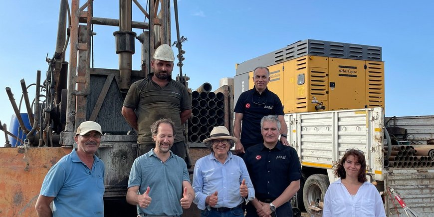 The group is standing in front of a smaller derrick that juts upwards out of the picture.