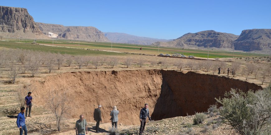 ein riesiges Erdloch in einer kargen Landschaft im Iran mit Bergen im Hintergrund