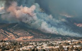 Fire with heavy smoke on wooded mountain slopes, a city in the valley.