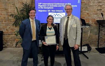 Photo of the award winner with the main organizers in front of a screen displaying the conference title