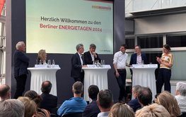 Audience and 6 panelists with a moderator on the podium (standing)